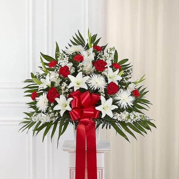 Standing floral spray with red roses, white lilies, and a red ribbon