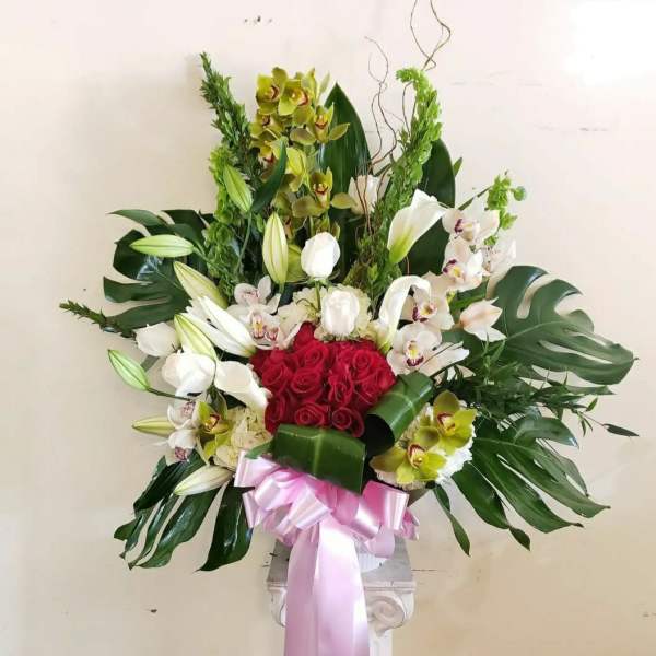 Large floral arrangement with red roses, white orchids, and lilies in a pedestal vase