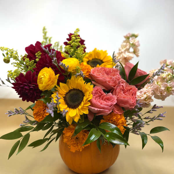 Mixed bouquet in a pumpkin vase with sunflowers, pink roses, and orange blooms