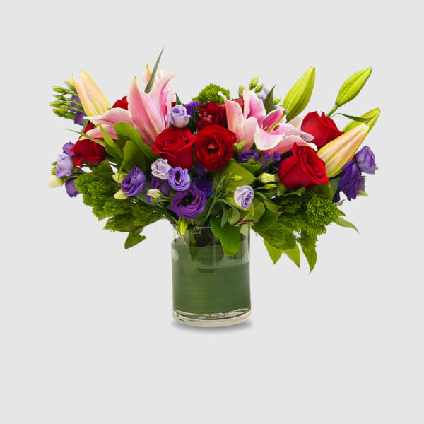 Bouquet of red roses, pink lilies, and purple blooms in a glass vase