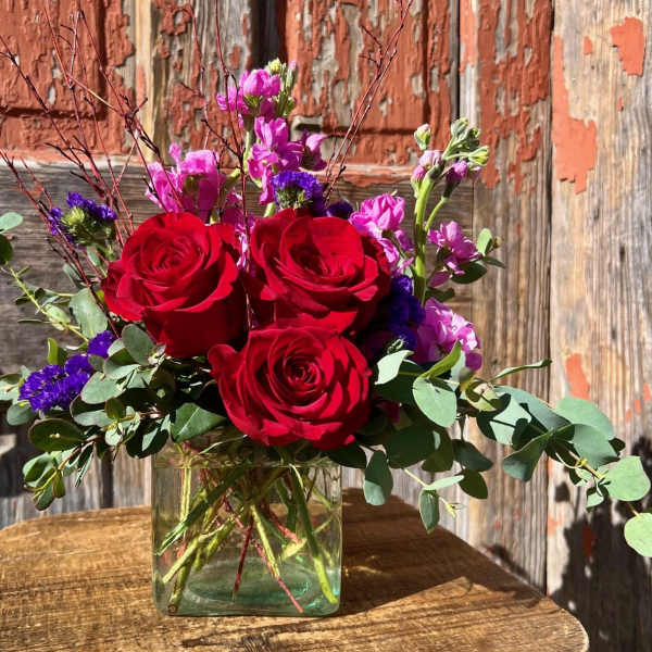 Red roses and purple flowers in a clear glass vase