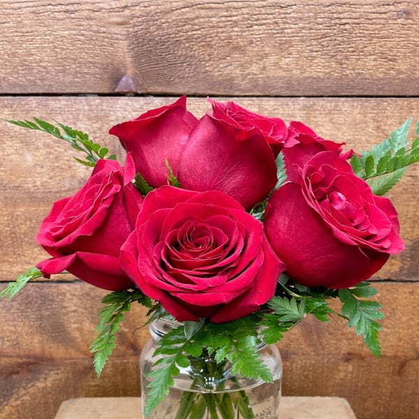 Red roses arranged in a clear glass jar vase