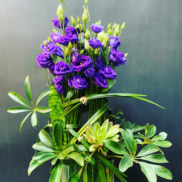 Purple lisianthus arrangement in a clear glass vase with green foliage