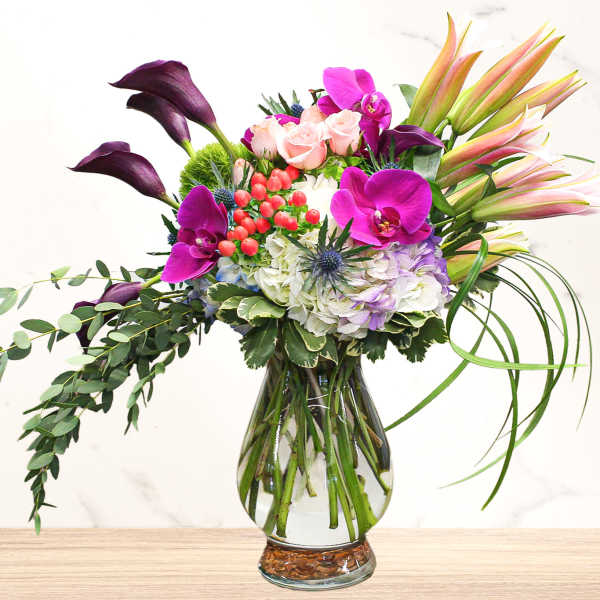 Mixed bouquet with purple orchids, pink roses, lilies, and hydrangea in a glass vase