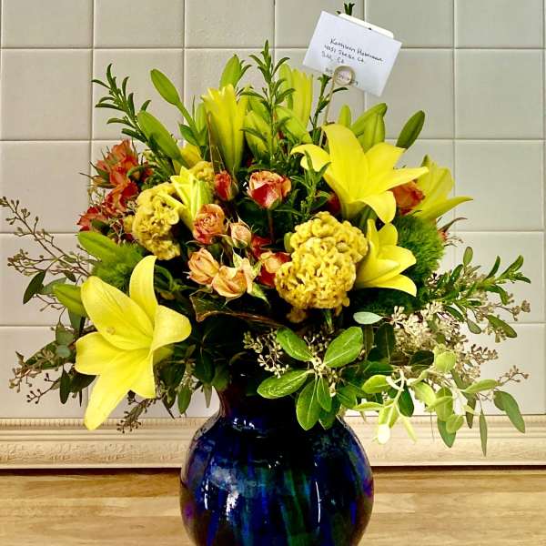 Yellow lilies and orange flowers arranged in a blue glass vase