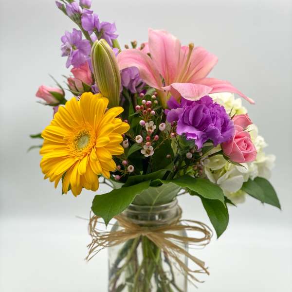 Mixed bouquet in a glass jar vase with pink, purple, yellow, and white blooms