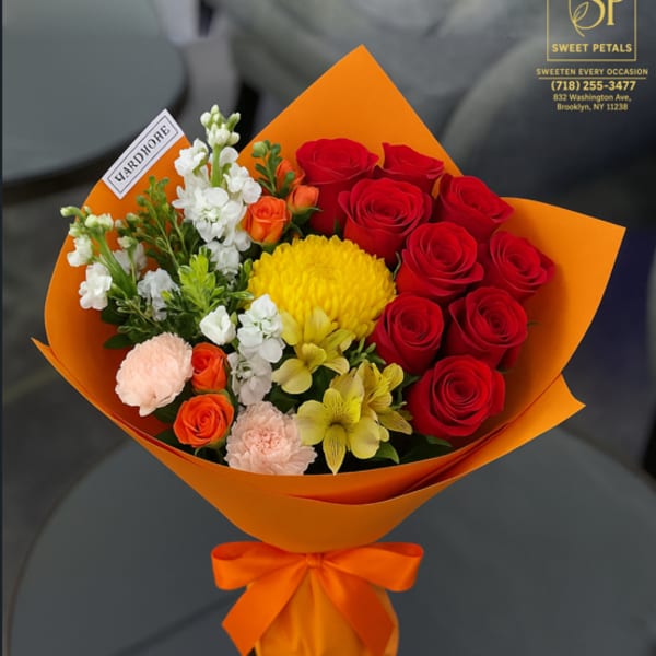 Bouquet of red roses, yellow blooms, and white flowers wrapped in orange paper