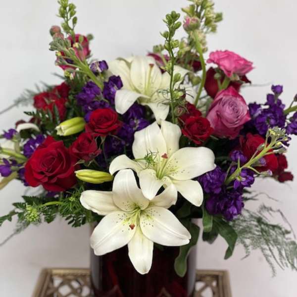Bouquet of white lilies, red and pink roses, and purple flowers in a dark vase