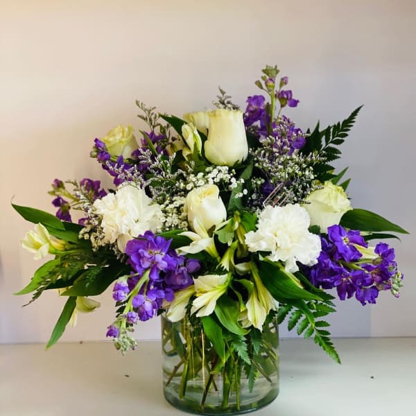 White roses and purple flowers arranged in a clear glass vase