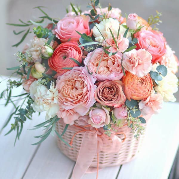 Pink and peach rose bouquet in a wicker basket with ribbon