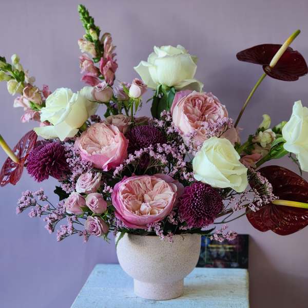 Pink and white floral arrangement in a white vase with burgundy anthuriums