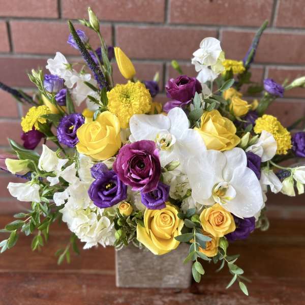 Bouquet of yellow, purple, and white flowers in a square vase