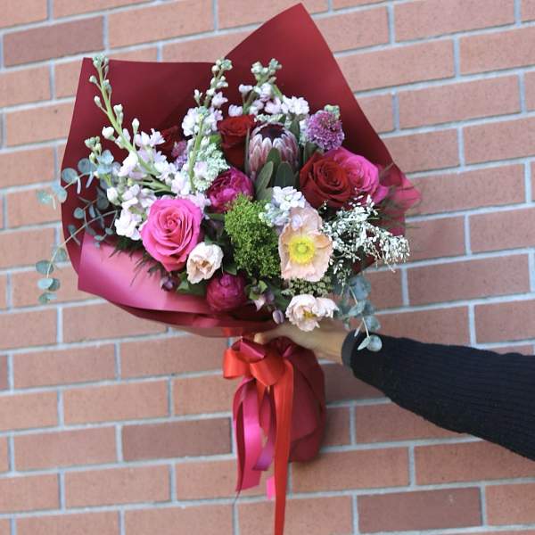 Handheld bouquet of pink and red roses with mixed blooms wrapped in burgundy paper