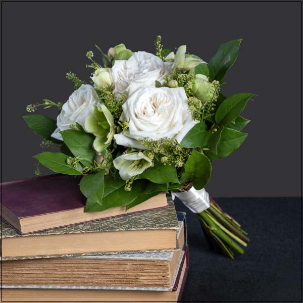 White rose bouquet with green accents resting on stacked books