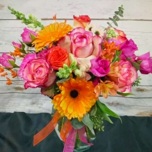 Bright mixed bouquet with pink roses and orange gerbera daisies in a glass vase