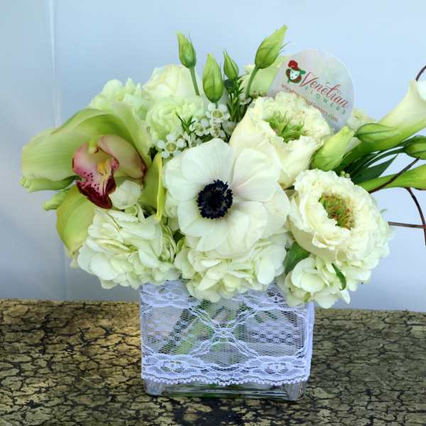 Low rectangular arrangement of white blooms with calla lilies in a glass vase wrapped in lace
