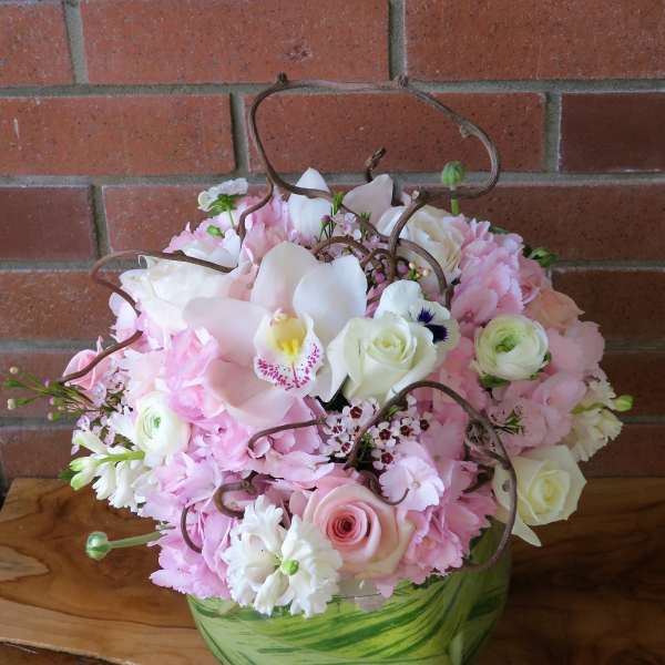 Pink and white floral arrangement in a green glass vase with curly branches
