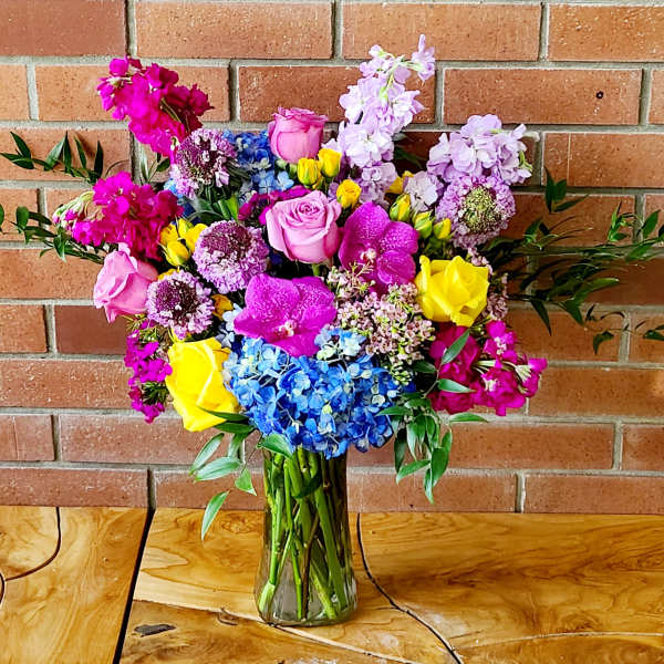 Colorful bouquet of roses, orchids, hydrangeas, and purple blooms in a glass vase