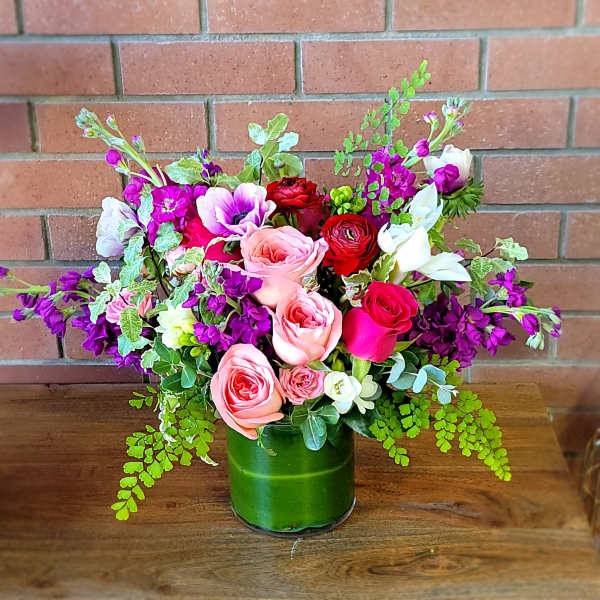 Mixed bouquet of pink, red, white, and purple flowers in a green glass vase
