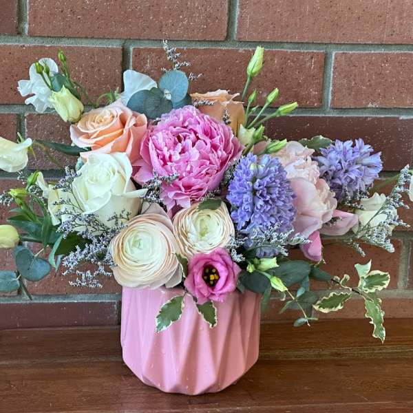 Pastel arrangement of roses, peonies, ranunculus and hyacinth in a pink ceramic vase