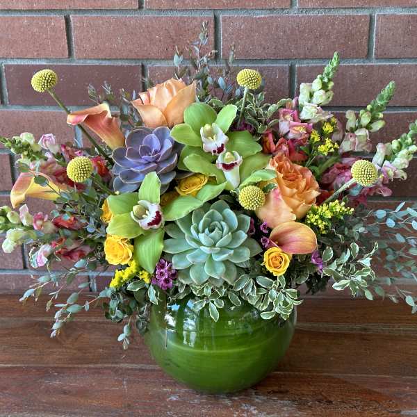 Mixed floral arrangement in a green glass vase with succulents and orchids
