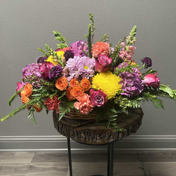 Colorful mixed flower arrangement in a wicker basket on a wood slab stand