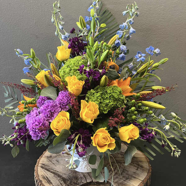 Bright mixed bouquet with yellow roses, purple carnations, and blue delphinium in a vase