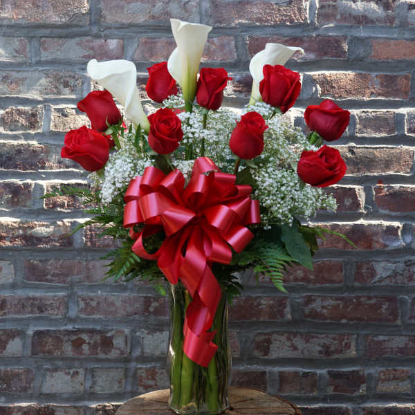 Red roses and white calla lilies in a glass vase with a red ribbon