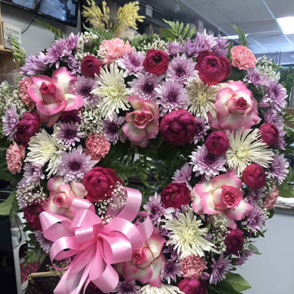 Heart-shaped floral wreath with pink and purple flowers and a pink ribbon bow