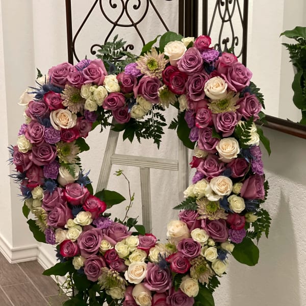 Heart-shaped floral wreath of pink, purple, and white roses on a stand