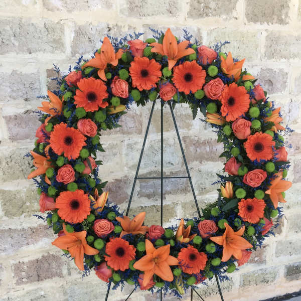 Circular floral wreath with orange lilies, gerbera daisies, and pink roses on a stand