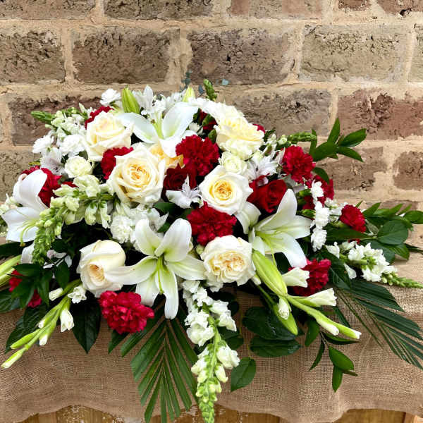 Red and white funeral spray with lilies, roses, carnations, and snapdragons in an elongated design