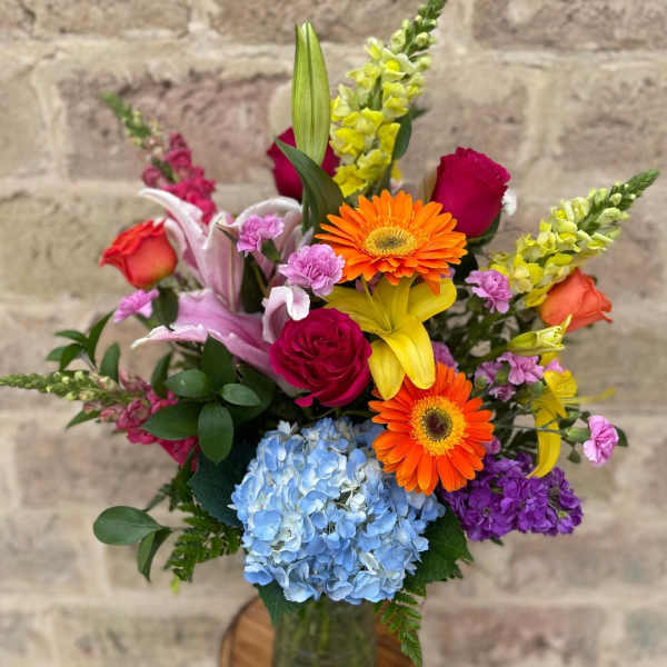 Colorful mixed bouquet in a glass vase with roses, lilies, gerbera daisies, and hydrangea