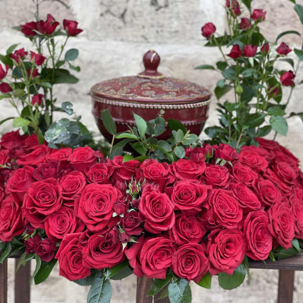 Heart-shaped arrangement of red roses with a decorative lidded box behind it