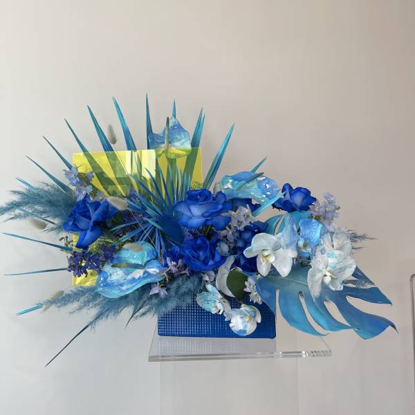 Blue floral arrangement with orchids and roses in a rectangular vase