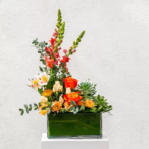 Mixed floral arrangement in a green glass vase with orange roses and pink snapdragons