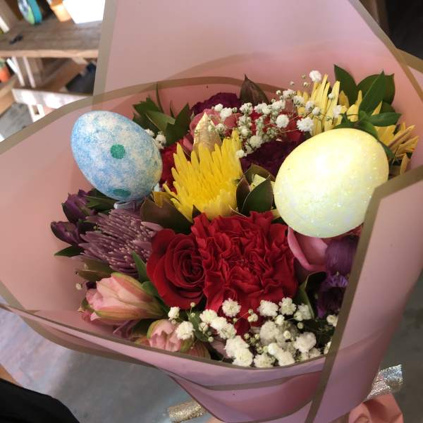 Hand-tied bouquet of bright mixed flowers with decorative pastel eggs wrapped in pink paper