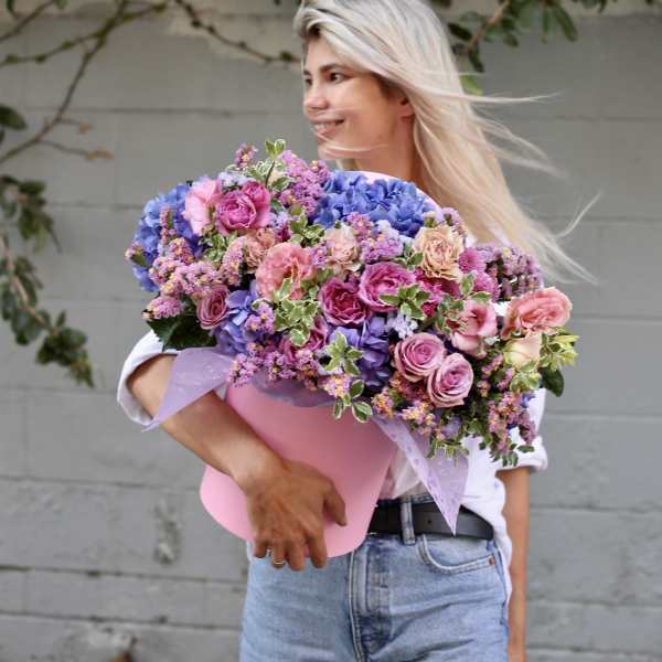 Woman holding a large bouquet of pink, purple, and blue flowers in a pink wrap
