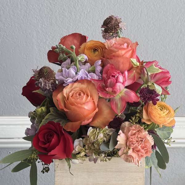 Mixed bouquet of roses, ranunculus, and carnations in a wooden box
