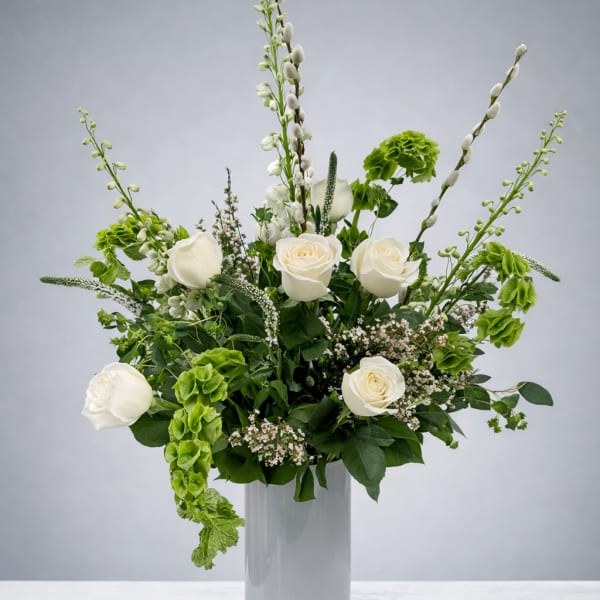 White roses and green blooms arranged in a tall glass vase