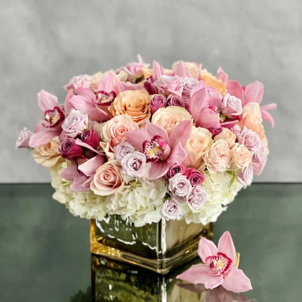 Pink and peach bouquet of roses and orchids in a square glass vase
