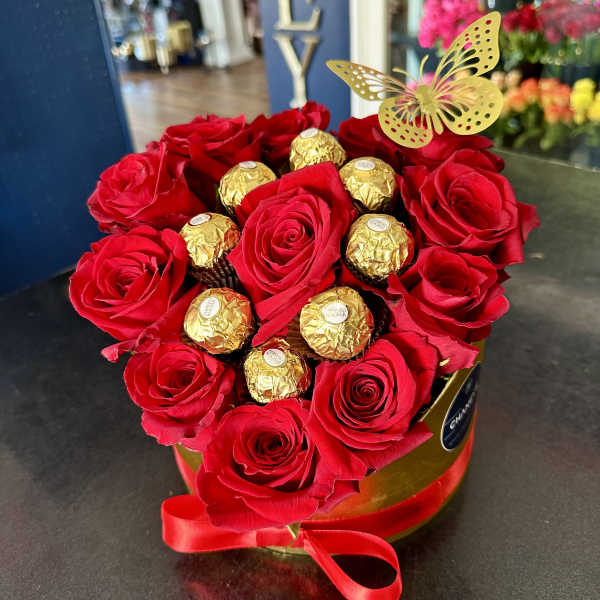 Red roses arranged with gold-wrapped chocolates in a round box