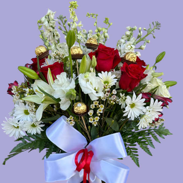 Bouquet of red roses, white lilies, and daisies in a glass vase with a ribbon