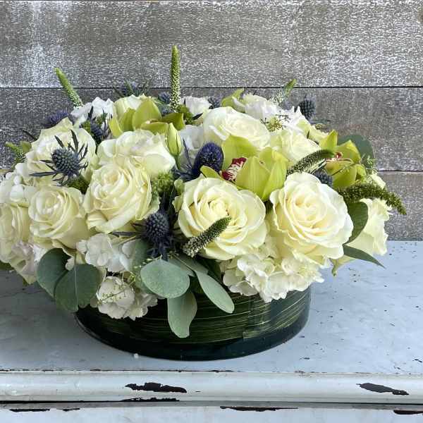 Low floral arrangement of white roses and green blooms in a round container