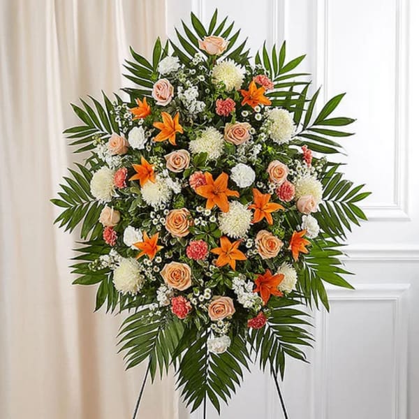 Standing floral spray with orange lilies, peach roses, and white blooms
