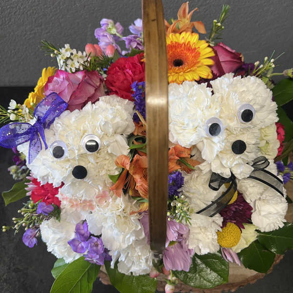 Basket of bright mixed flowers with two white carnation dog figures decorated with googly eyes and bows