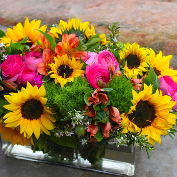 Bright bouquet of sunflowers, pink roses, and orange blooms in a glass vase