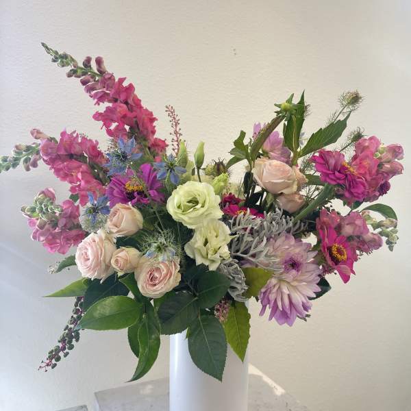 Mixed pink and lavender flowers arranged in a tall white vase