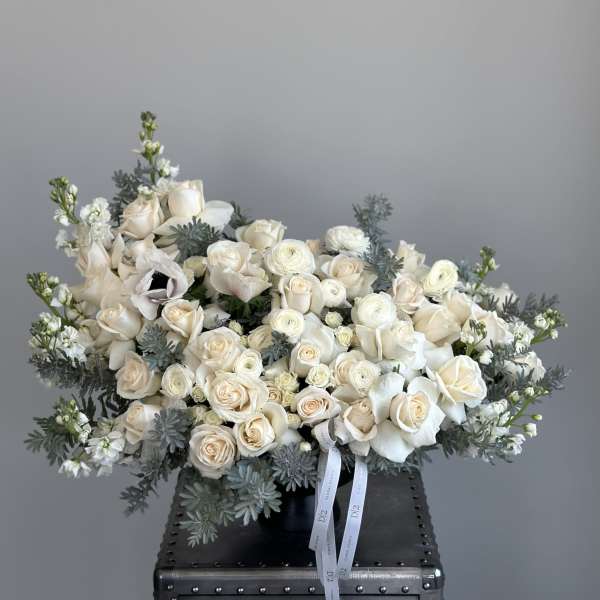 Cream rose bouquet with white blooms and blue-gray foliage in a black vase