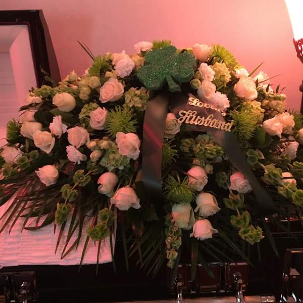 Large funeral wreath of pale pink roses and white flowers with a black ribbon